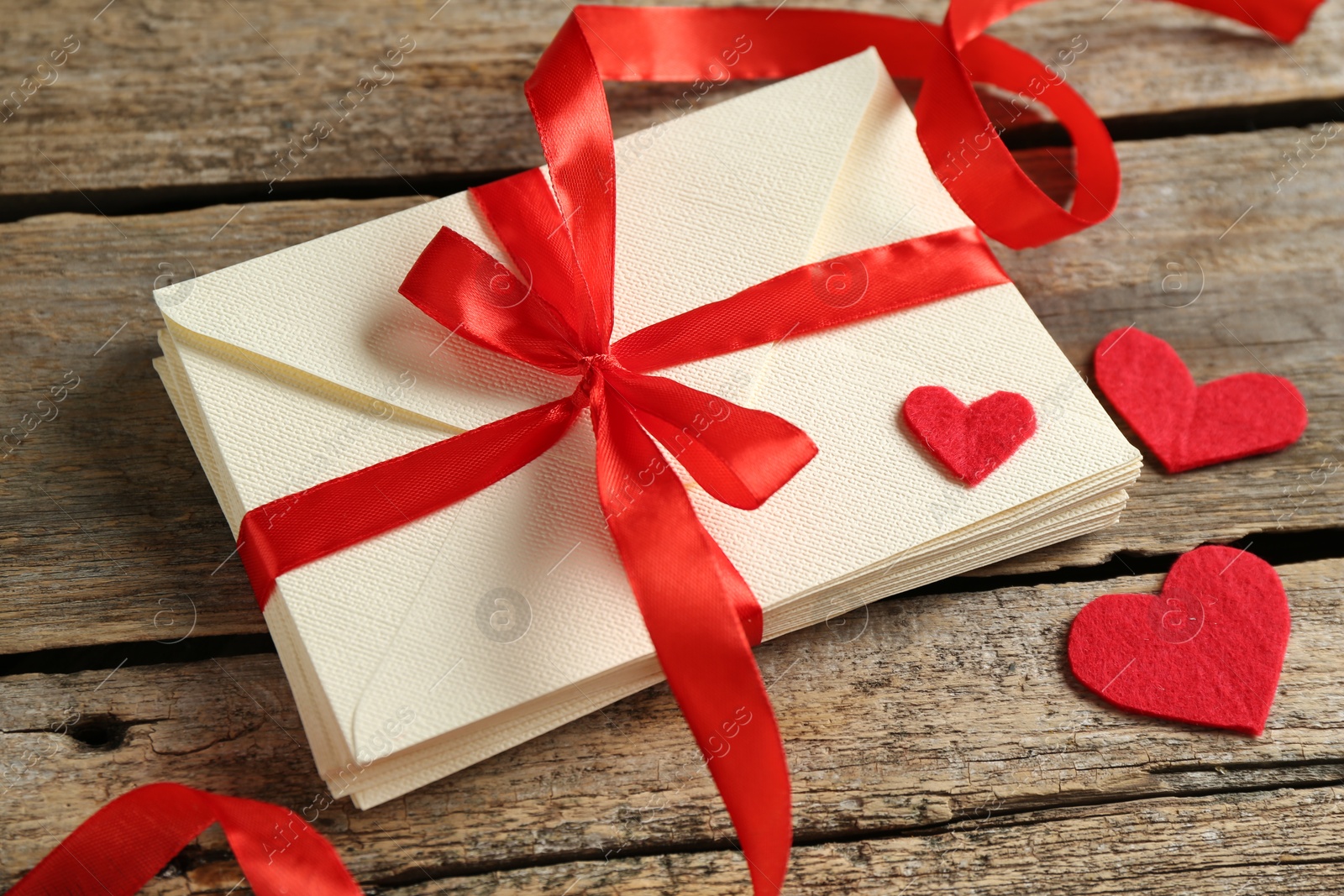 Photo of Stack of love letters and paper hearts on wooden table, closeup