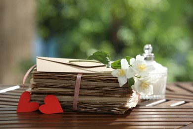 Photo of Stack of love letters, paper hearts and flowers on wooden table, closeup. Space for text