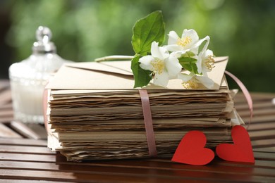Photo of Stack of love letters, paper hearts and flowers on wooden table, closeup