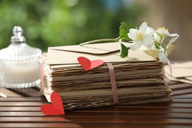 Photo of Stack of love letters, paper hearts and flowers on wooden table, closeup