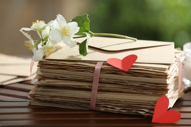 Photo of Stack of love letters, paper hearts and flowers on wooden table, closeup