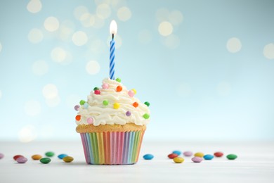 Photo of Burning candle in cupcake and candies on table against blue background with blurred lights. Space for text