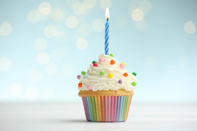 Photo of Burning candle in cupcake on table against blue background with blurred lights