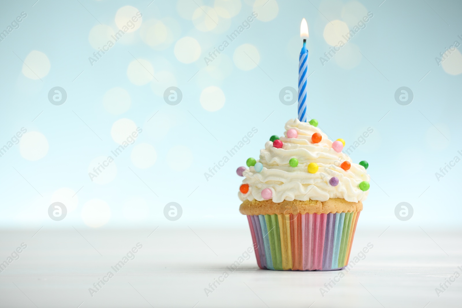 Photo of Burning candle in cupcake on table against blue background with blurred lights. Space for text