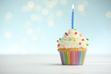Photo of Burning candle in cupcake on table against blue background with blurred lights. Space for text
