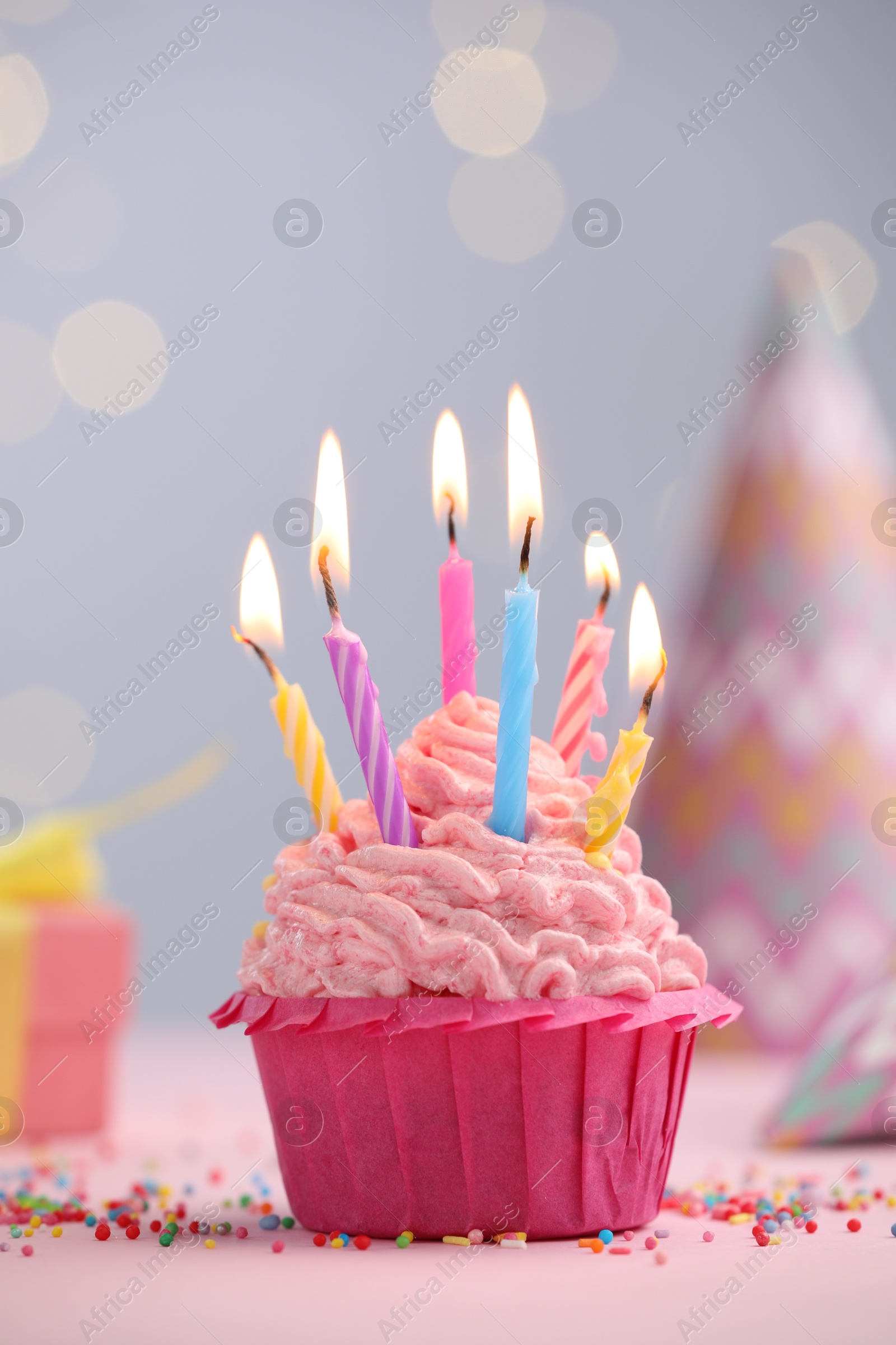 Burning candles in cupcake, sprinkles and party decor on table against blurred lights Photo of Burning candles in cupcake, sprinkles and party decor on table against blurred lights