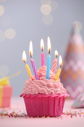 Photo of Burning candles in cupcake, sprinkles and party decor on table against blurred lights