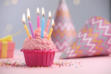 Photo of Burning candles in cupcake, sprinkles and party decor on table against blurred lights