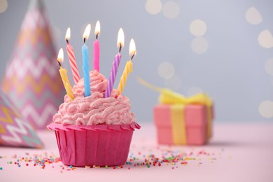 Photo of Burning candles in cupcake, sprinkles and party decor on table against blurred lights. Space for text