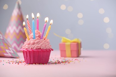 Photo of Burning candles in cupcake, sprinkles and party decor on table against blurred lights. Space for text