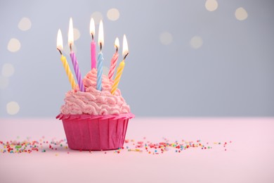 Photo of Burning candles in cupcake and sprinkles on table against blurred lights. Space for text