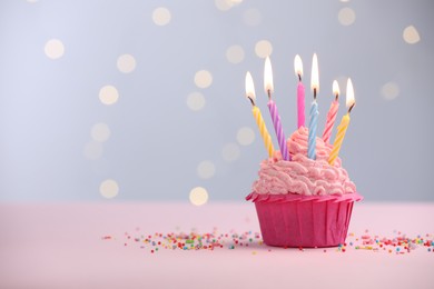 Photo of Burning candles in cupcake and sprinkles on table against blurred lights. Space for text