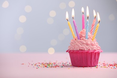 Photo of Burning candles in cupcake and sprinkles on table against blurred lights. Space for text