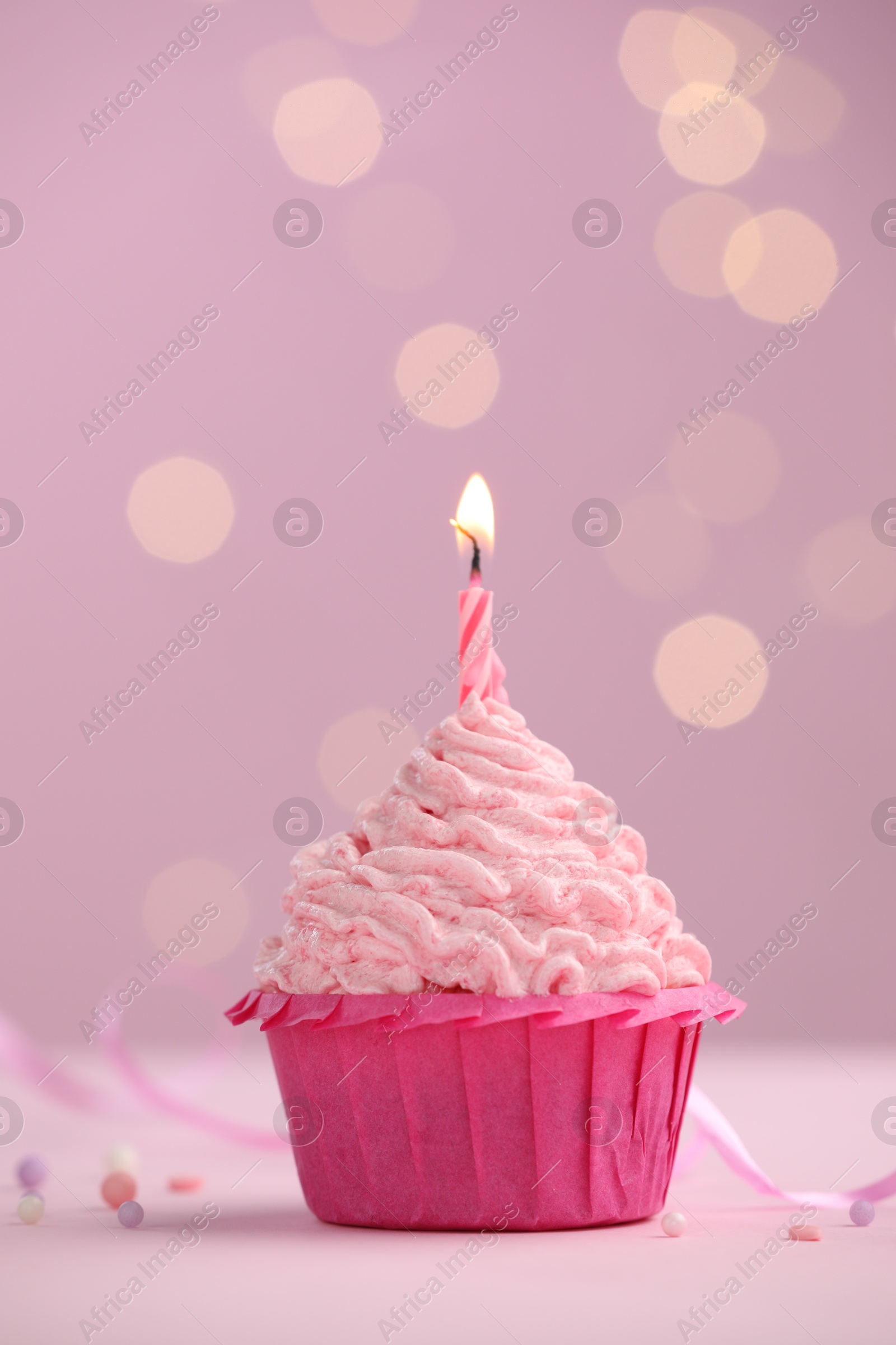 Photo of Burning candle in cupcake on table against pink background with blurred lights. Space for text