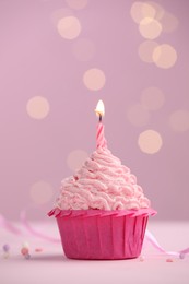 Photo of Burning candle in cupcake on table against pink background with blurred lights. Space for text