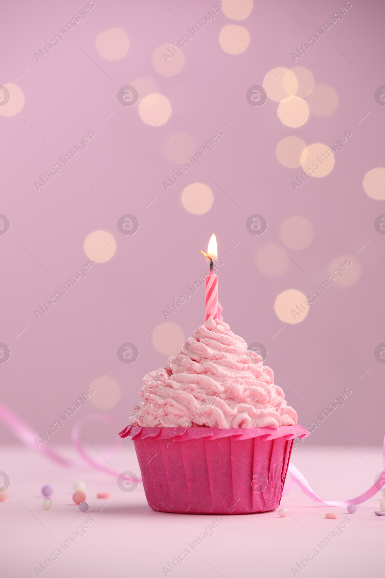 Burning candle in cupcake on table against pink background with blurred lights. Space for text Photo of Burning candle in cupcake on table against pink background with blurred lights. Space for text