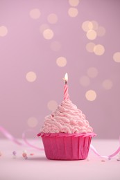 Photo of Burning candle in cupcake on table against pink background with blurred lights. Space for text