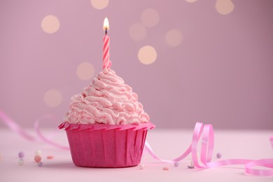 Photo of Burning candle in cupcake on table against pink background with blurred lights. Space for text
