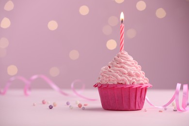 Photo of Burning candle in cupcake on table against pink background with blurred lights. Space for text