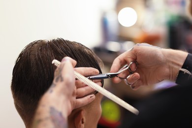 Photo of Professional barber cutting client's hair with scissors in barbershop, closeup