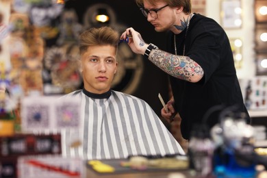 Photo of Professional barber cutting client's hair with scissors in barbershop