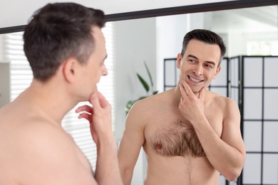 Photo of Smiling man after shaving looking at mirror in bathroom