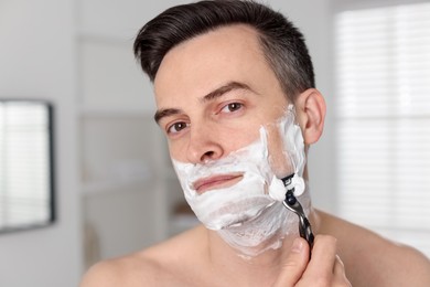 Photo of Handsome man shaving with razor at home