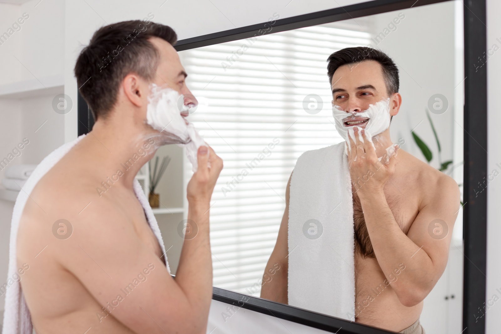 Smiling man applying shaving foam near mirror in bathroom Photo of Smiling man applying shaving foam near mirror in bathroom