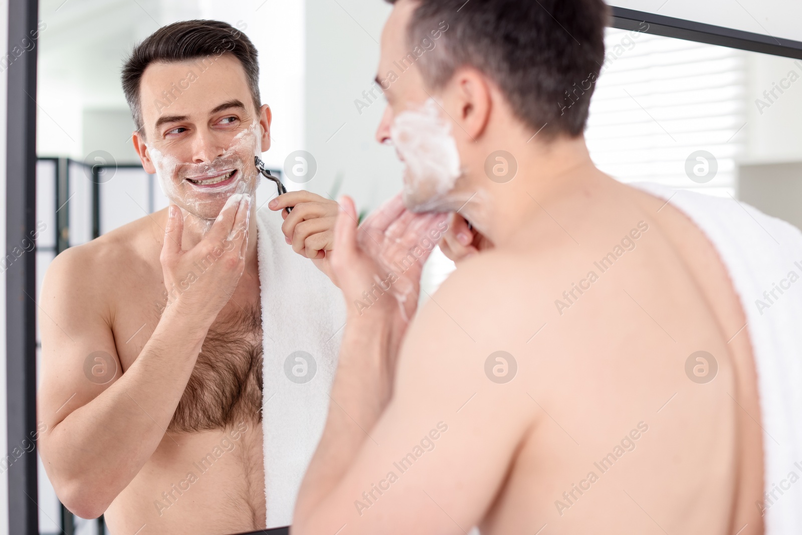 Smiling man applying shaving foam near mirror in bathroom Photo of Smiling man applying shaving foam near mirror in bathroom