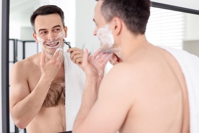 Photo of Smiling man applying shaving foam near mirror in bathroom