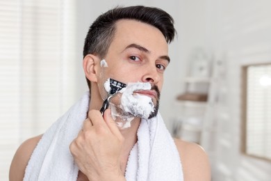 Photo of Handsome man shaving with razor at home