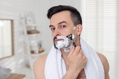 Photo of Handsome man shaving with razor at home