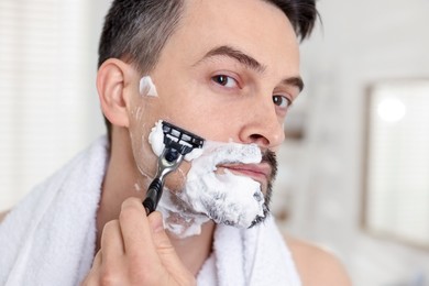 Photo of Handsome man shaving with razor at home, closeup