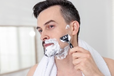 Photo of Handsome man shaving with razor at home, closeup