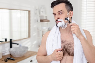 Photo of Handsome man shaving with razor in bathroom