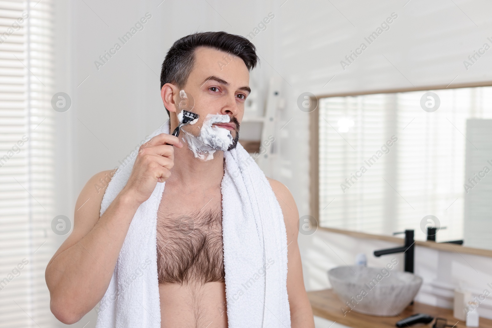 Photo of Handsome man shaving with razor in bathroom