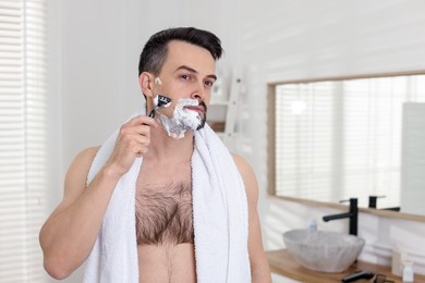Photo of Handsome man shaving with razor in bathroom