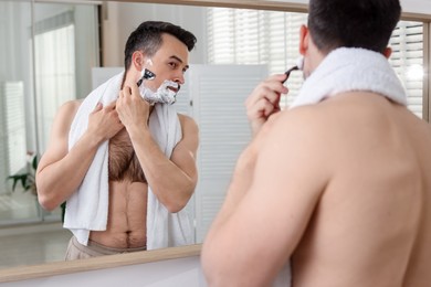 Photo of Handsome man shaving with razor near mirror at home