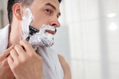Photo of Handsome man shaving with razor at home. Space for text