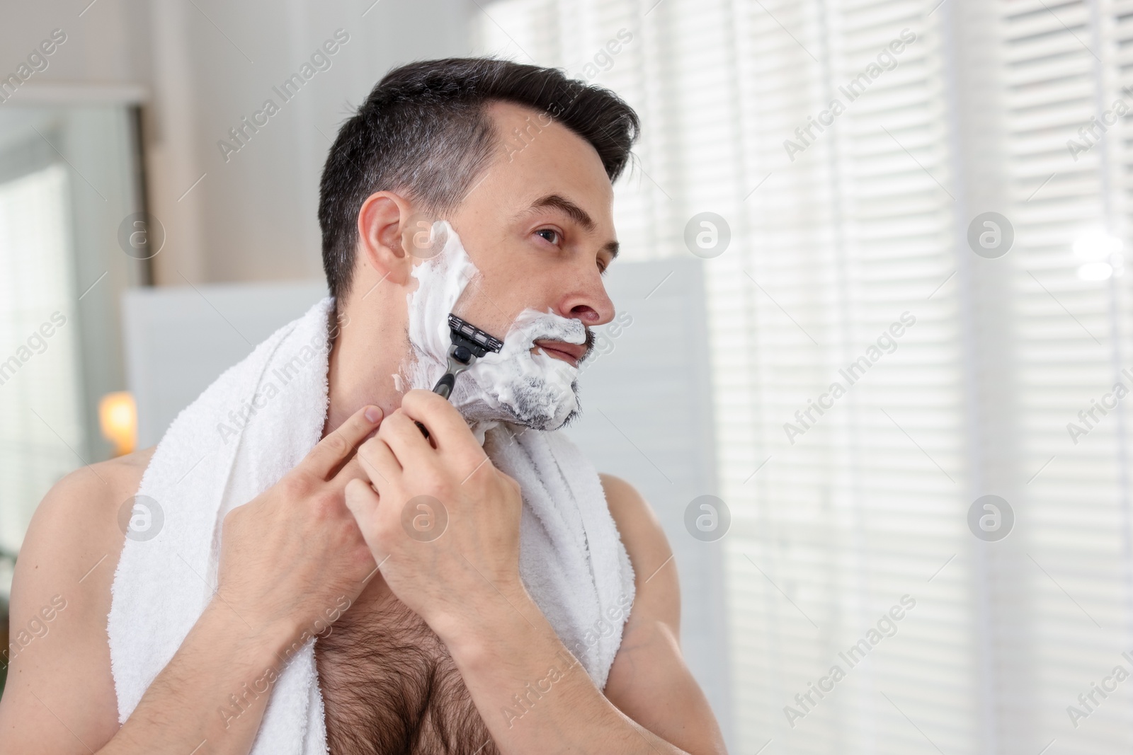 Photo of Handsome man shaving with razor at home. Space for text