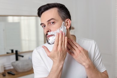 Photo of Handsome man applying shaving foam in bathroom