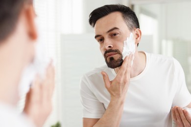 Photo of Handsome man applying shaving foam near mirror in bathroom
