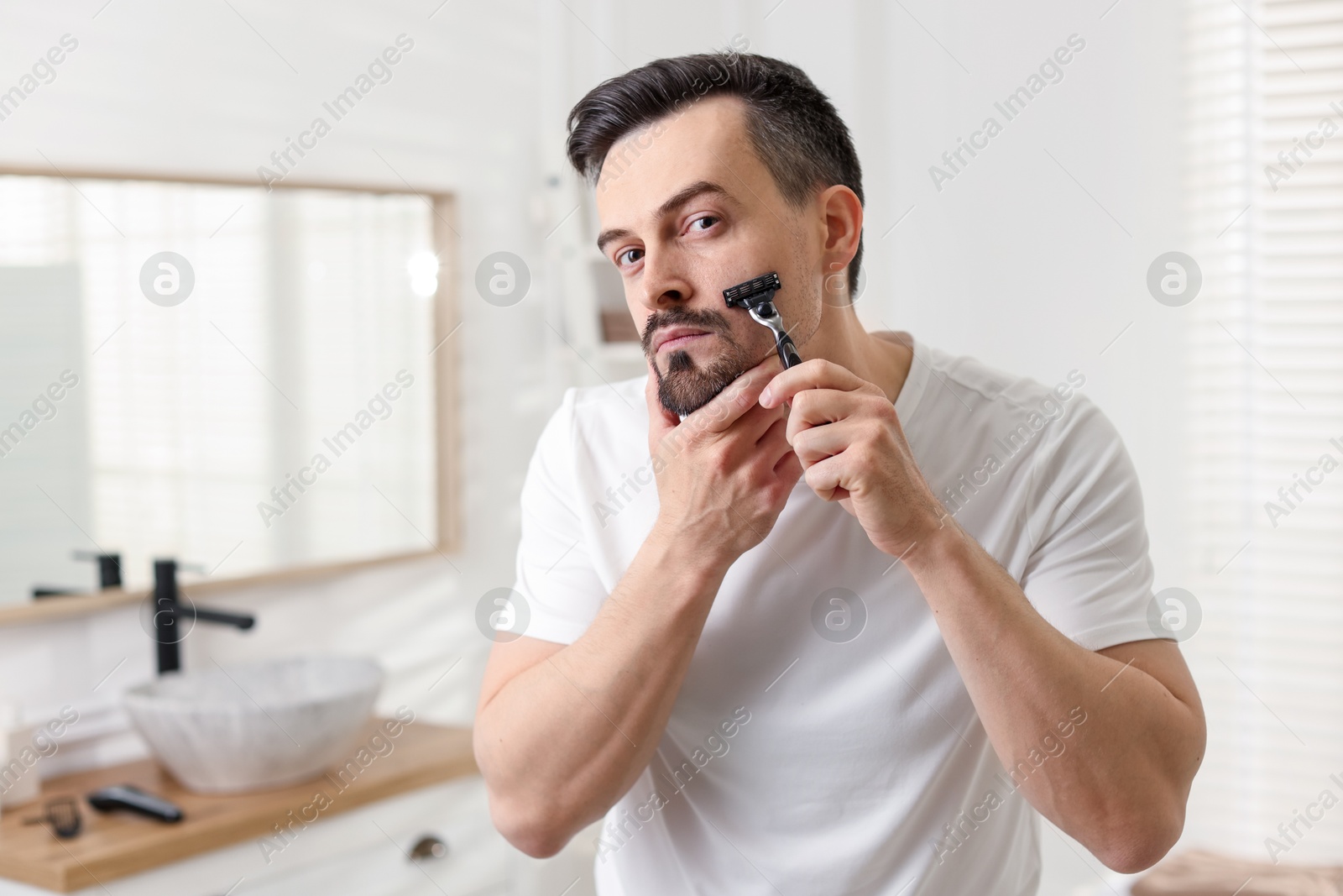 Handsome man shaving with razor in bathroom Photo of Handsome man shaving with razor in bathroom