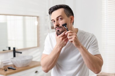 Photo of Handsome man shaving with razor in bathroom