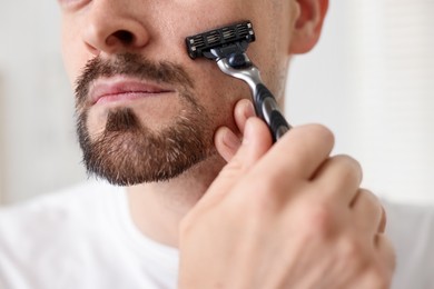 Photo of Man shaving with razor at home, closeup