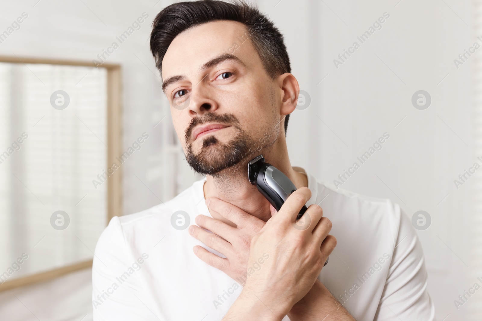 Photo of Handsome man shaving with trimmer at home