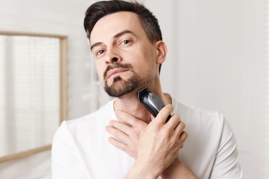 Photo of Handsome man shaving with trimmer at home