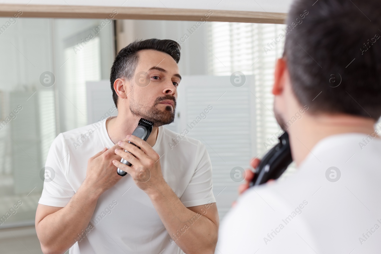 Handsome man shaving with trimmer near mirror at home Photo of Handsome man shaving with trimmer near mirror at home