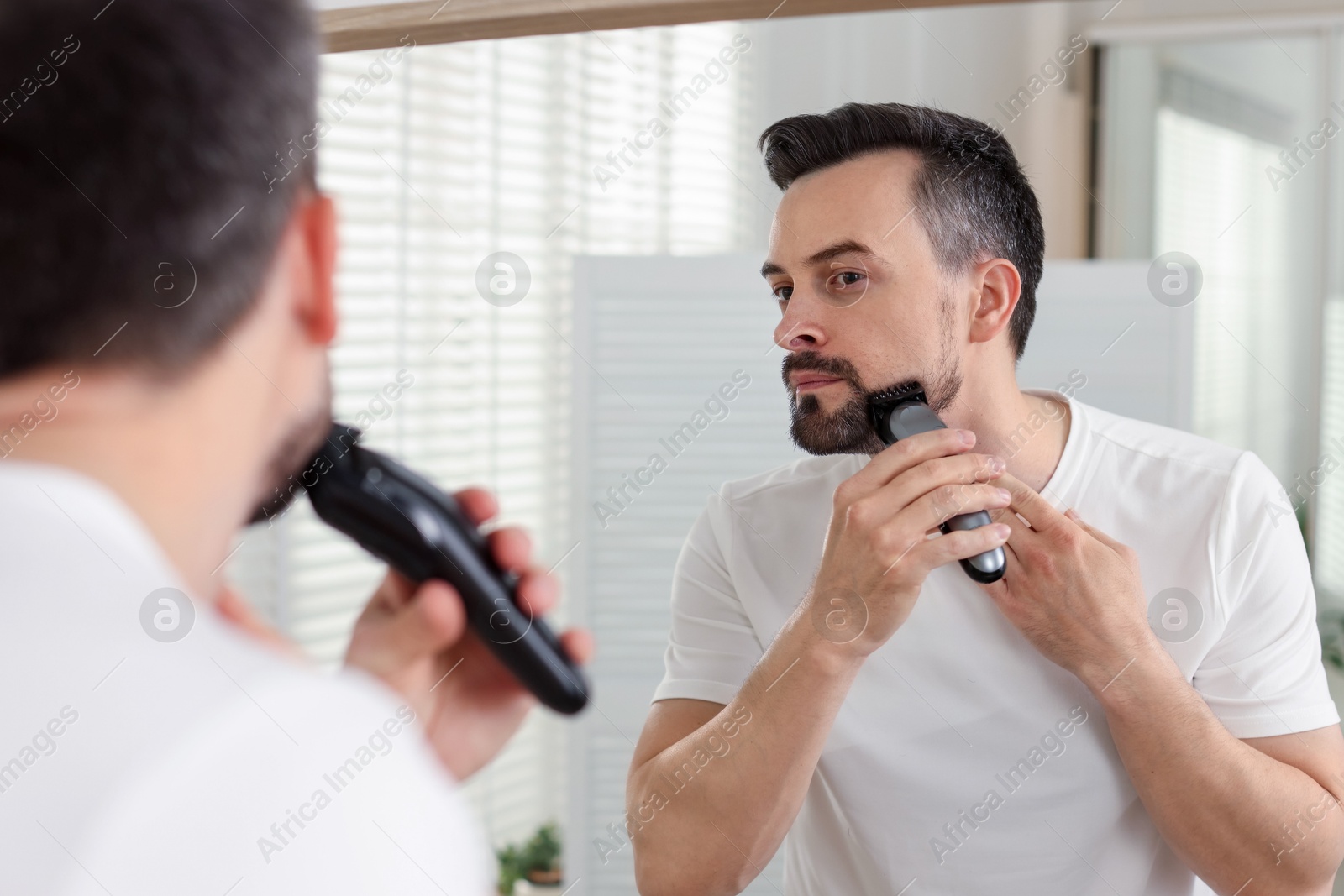 Handsome man shaving with trimmer near mirror at home Photo of Handsome man shaving with trimmer near mirror at home
