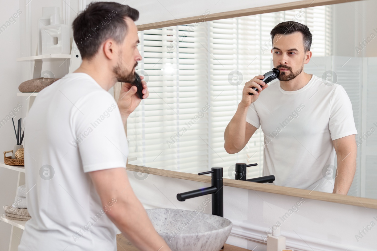 Handsome man shaving with trimmer near mirror at home Photo of Handsome man shaving with trimmer near mirror at home